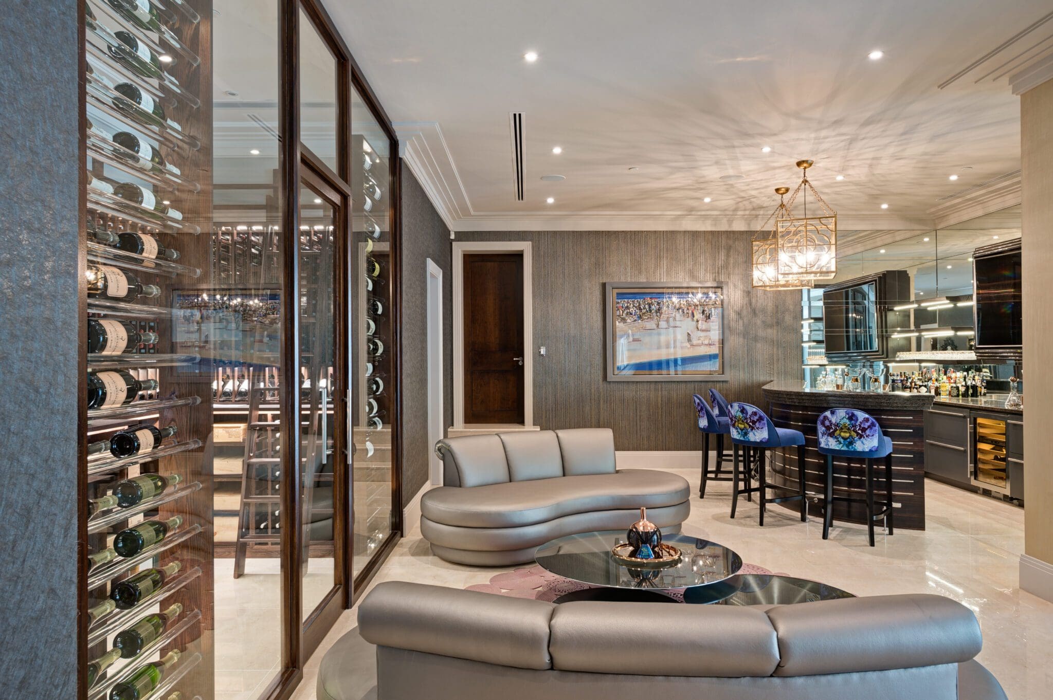 Modern living area with a curved sofa, glass wine storage, high chairs, and a bar. The space becomes a home with sleek decor and a large framed painting on the wall.
