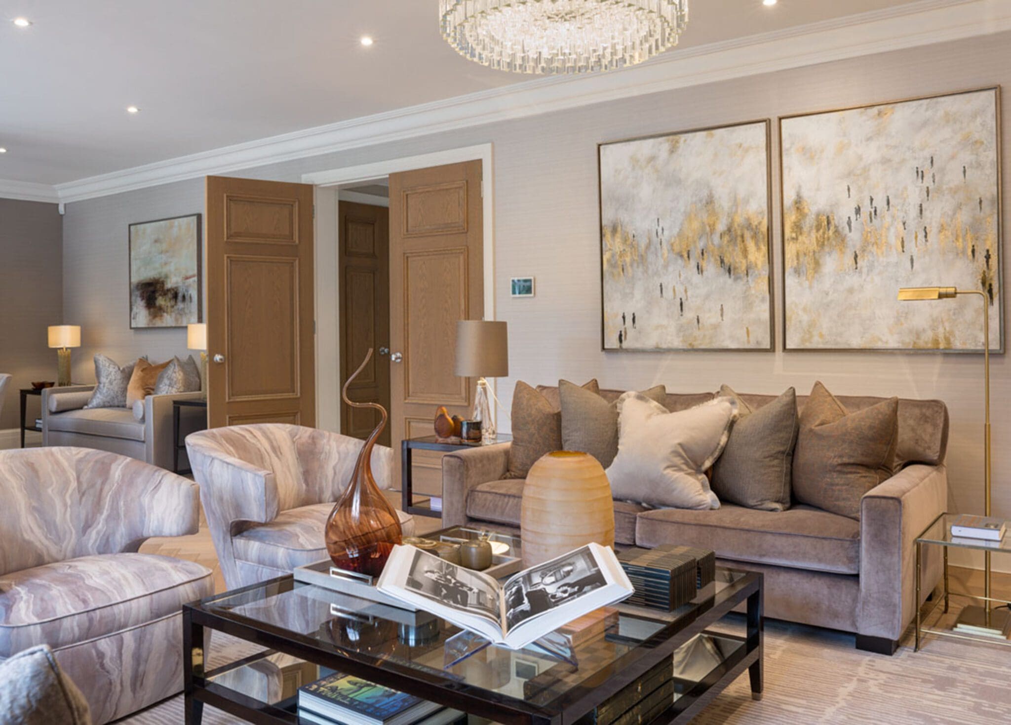 Modern living room with a brown sofa, abstract art on the wall, glass coffee table with decorative items, and an open doorway leading to another room.