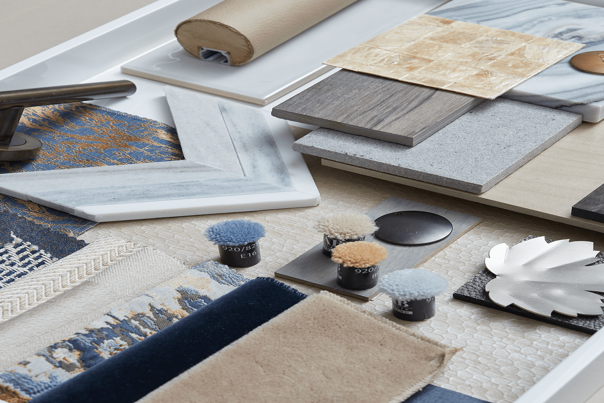 A meticulously curated collection of interior design materials, including fabric swatches, tiles, and metallic accents, is organized on a tray. Ideal for enhancing interior design vision with a touch of elegance.
