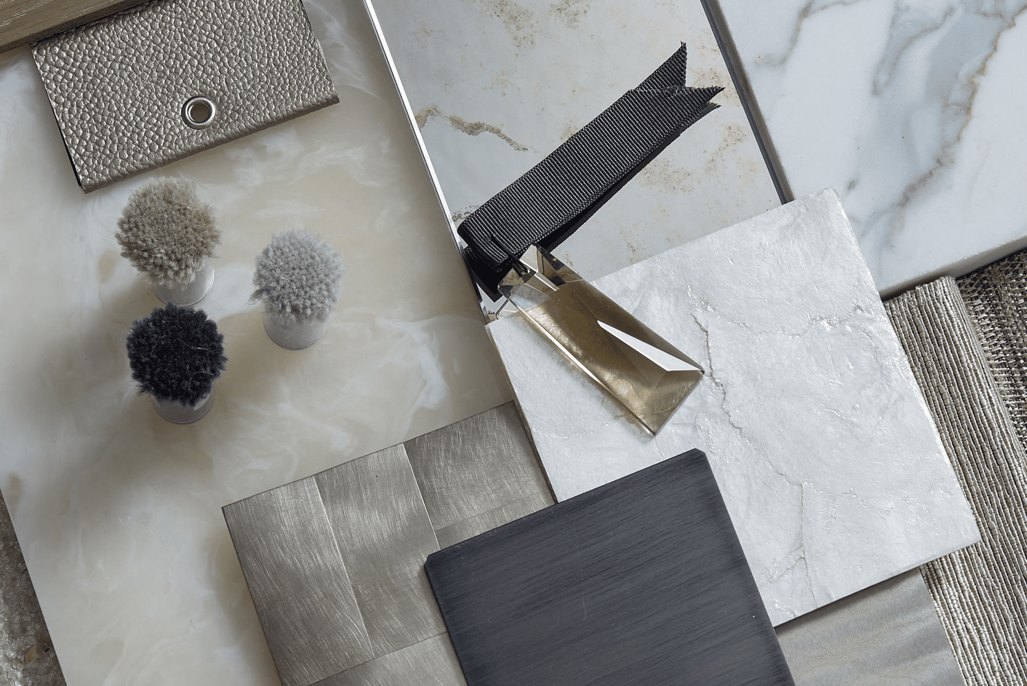 An expertly curated collection of textured material samples, featuring fabric swatches, metal hardware, and a variety of stone and tile surfaces, all meticulously arranged on a flat surface to serve as the ideal layout of a luxury interior design