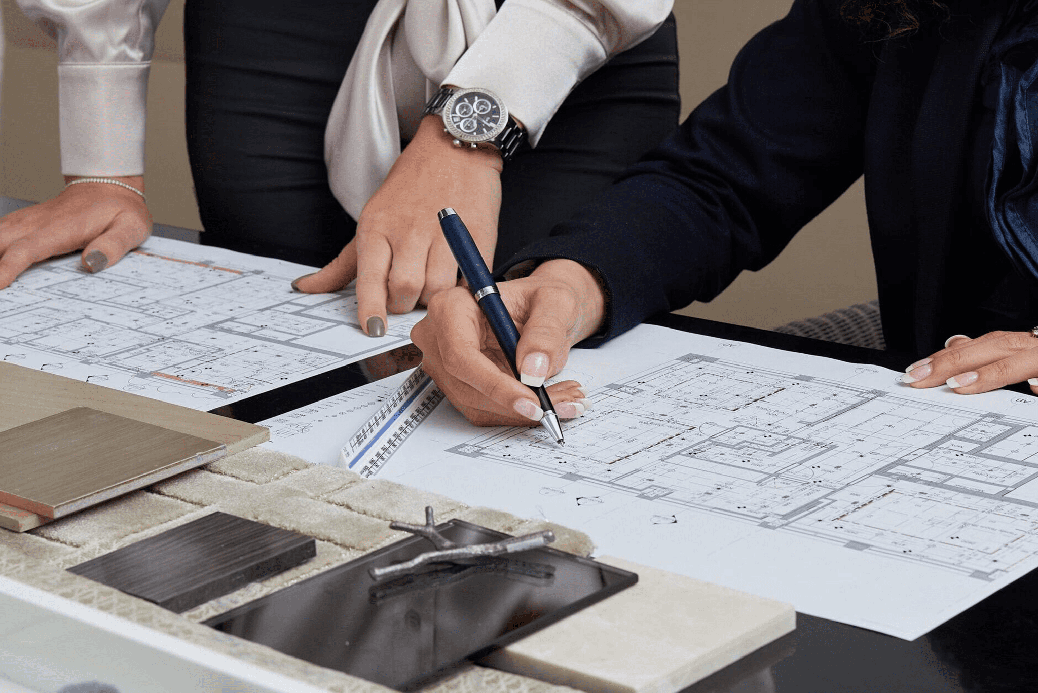 Two people reviewing architectural blueprints on a table, surrounded by material samples and a pencil. One person is pointing with a pen, considering the design's header template for enhanced clarity.