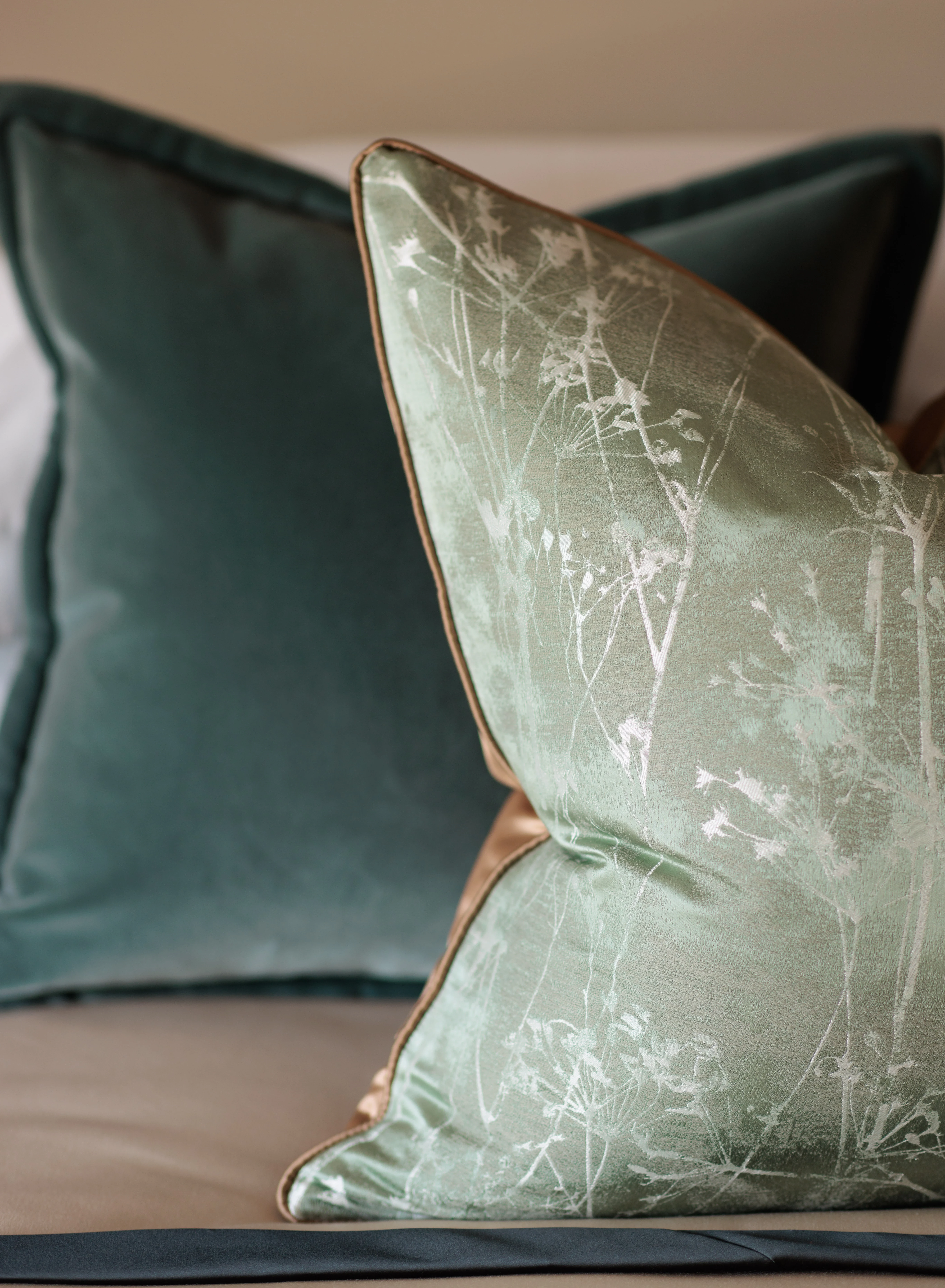 Close-up of two decorative pillows, one in light green with a floral pattern and one in solid dark green, placed on a beige surface.